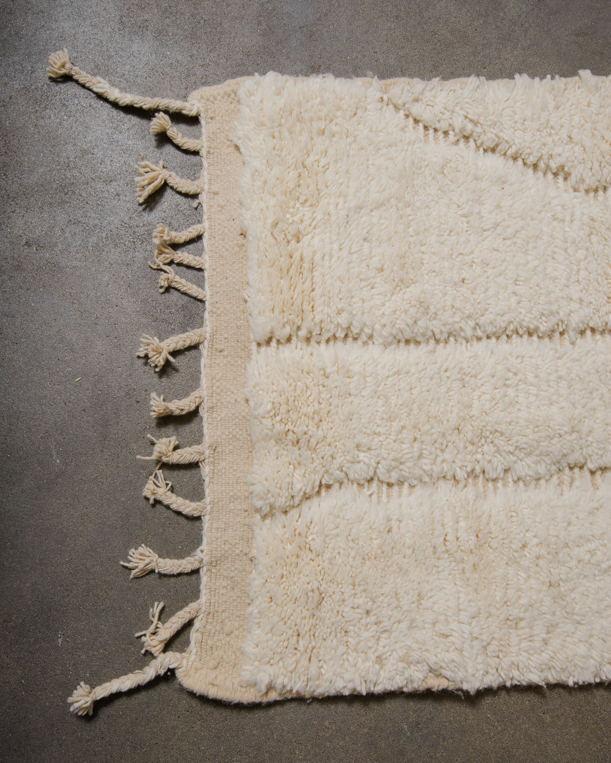 One end of Berber runner rug with a tightly woven edge and natural wool tassels.
